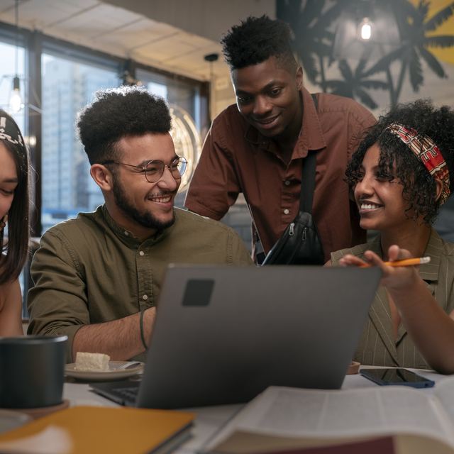 Four young colleagues smiling and talking together around a laptop.