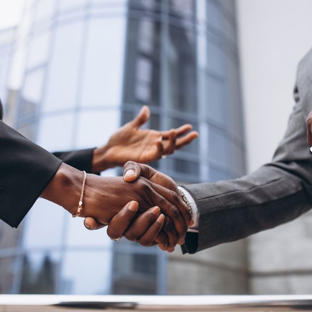 Two people in business suits shaking hands outside an office building.