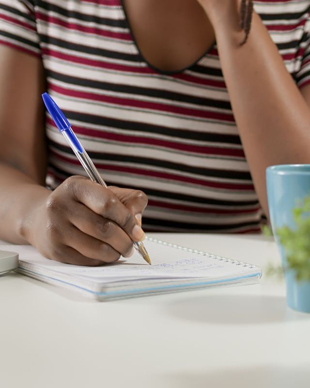 A person writing notes in a notebook at a bright desk.